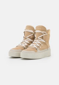 Sneakers beige alte con suole bianche spesse, lacci bianchi, texture in suede e una morbida fodera in pelliccia interna.