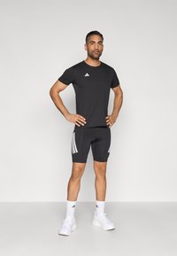 Czarny sportowy t-shirt i spodenki z białymi trzema paskami. Tkanina jest gładka, elastyczna i dopasowana dla komfortu podczas ćwiczeń.