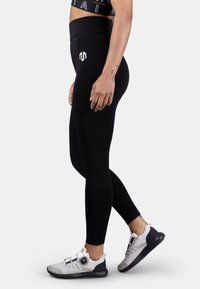 Black leggings made of stretchy fabric, featuring a high waistband. Accompanied by gray and black athletic shoes with adjustable hardware.