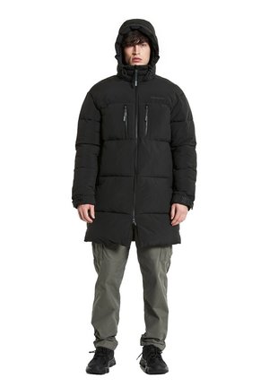 Schwarze Steppjacke mit Kapuze, Reißverschluss vorne, zwei Brusttaschen und gestepptem Design, kombiniert mit olivfarbener Cargo-Hose und schwarzen Turnschuhen.