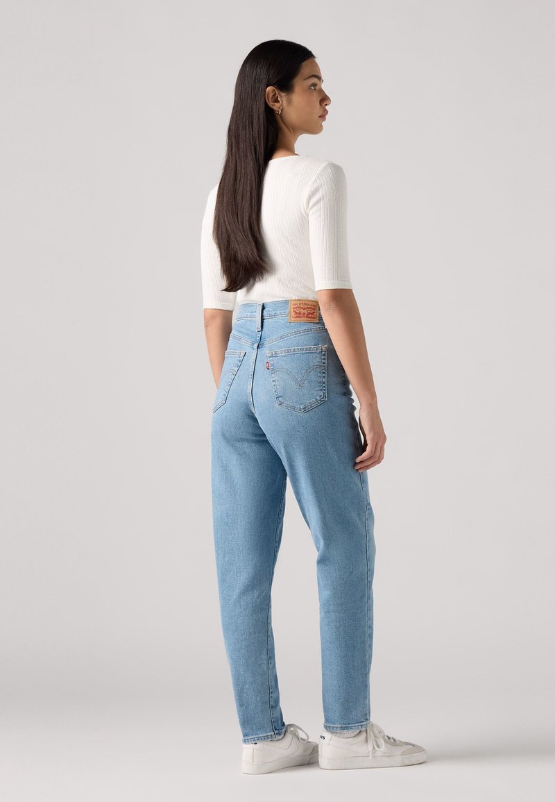 Helles, blaues Denim mit hoher Taille, geradem Bein und sichtbaren Gesäßtaschen. Mit einem hellbraunen Lederetikett am Bund.