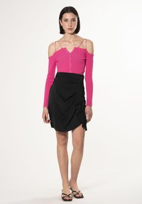 Maglione fucsia a coste con design off-shoulder, dettagli con bottoni, abbinato a una gonna nera avvolgente con rouches e un dettaglio a fiocco.