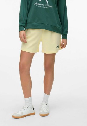 Gele katoenen korte broek met een relaxed fit, voorzien van een geborduurd ontwerp, gecombineerd met een groene sweatshirt en witte sneakers.