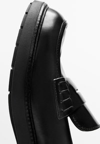 Czarny skórzany but z zaokrąglonym noskiem, wyposażony w pasek i klamrę. Podeszwa jest teksturowana, o grubym, żłobkowanym wzorze.