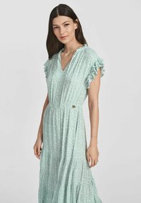 Jasnozielona sukienka w kwiatowy wzór z falbanami przy rękawach, dekoltem w serek i marszczoną talią; wykonana z teksturowanej tkaniny z warstwowym dołem.