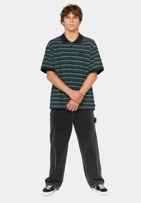 Camisa polo de rayas negras y verdes con manga corta, combinada con pantalones amplios negros y zapatillas negras. Diseño simple y casual.