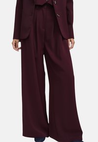 Pantaloni bordeaux a gamba larga in tessuto liscio, con vita alta, pieghe frontali e due tasche laterali.