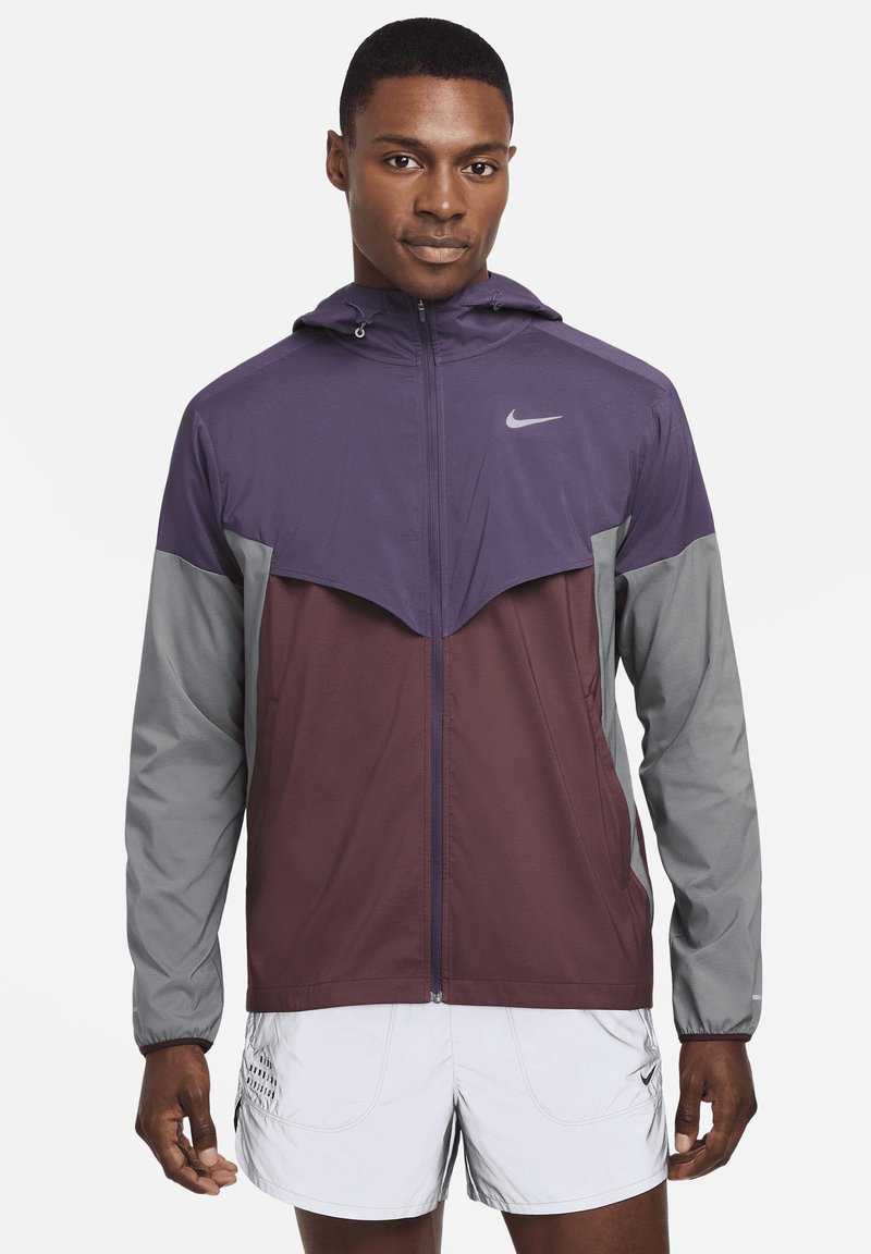 Chaqueta a bloques de color en púrpura, marrón y gris. Cuenta con un cierre frontal, capucha y puños elásticos. Confeccionada en un tejido ligero y texturizado.