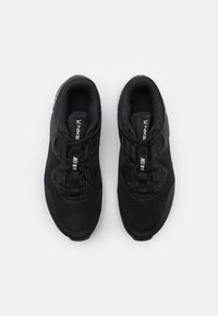 Para czarnych butów do biegania Nike z białymi podeszwami i napisem "Just Do It" na pętlach języka, widziana z góry na białym tle.