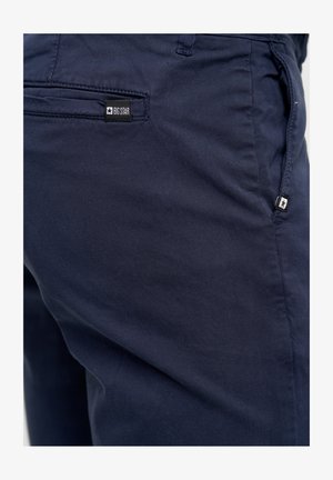 Dark navy trousers made of smooth fabric, featuring a small black label with white text and star logo near the back pocket.
