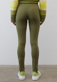 Olivgröna leggings i ett stretchigt, slätt material med en figurnära design. Bärs med klumpiga vita sneakers med gröna detaljer.