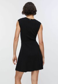 Abito nero a coste con corpetto aderente e gonna a ruota. Presenta un design senza maniche e dettagli decorativi in metallo sulle spalle.