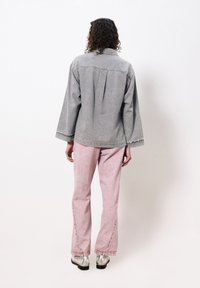 Graue Jeansjacke mit lockerer Passform und rückseitigem Faltenwurf, kombiniert mit hellrosa ausgestellten Jeans. Das Outfit hat ausgefranste Saumdetails und metallische Schuhe.