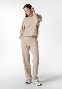 Beige lounge set med avslappnad passform, inklusive sweatshirt med ribbad mudd och matchande sweatpants med sidfickor och en mjuk yta.
