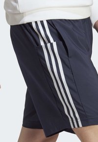 Námořnické sportovní šortky vyrobené z lehkého materiálu s bílými bočními pruhy a boční kapsou. Elastický pas pro pohodlí a flexibilitu.