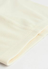 Cremefarvet stof med en ribbet tekstur, der viser foldede kanter og synlig syning, hvilket skaber et blødt udseende.