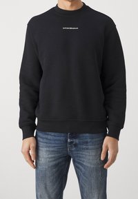 Musta puuvillainen collegepaita pyöreällä pääntiellä ja resoreilla hihoissa. Edessä pieni valkoinen "EMPORIO ARMANI" -logo. Yhdistetty sinisiin farkkuihin.