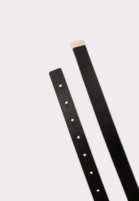 Sorte læderurrem med struktureret overflade, flere justeringshuller og en metalspænde med indgraveret branding.