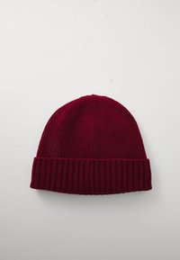 Burgundi színű bordázott kötött sapka hajtott szélekkel, fehér felületen fekve.