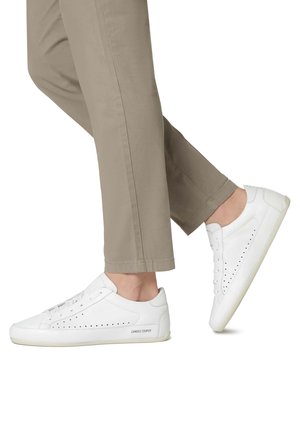 Zapatillas de cuero blancas con detalles perforados, suelas de goma planas y una textura suave. Combinadas con pantalones recortados de color beige claro.