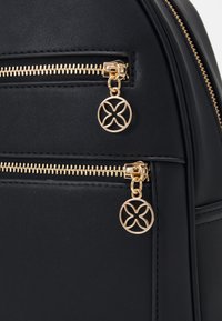 Bolso de piel sintética negra con dobles cremalleras doradas y tiradores circulares decorativos, además de un acabado texturizado. Forma estructurada con detalles de costura sutiles.