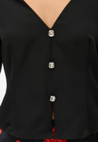 Must pluus sügava V-kaelusega, millel on ees hõbedased ruudukujulised nupud. Sile tekstuur ja kerge läige.