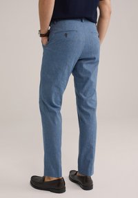 Lichtblauwe broek met een subtiele textuur, een getailleerde pasvorm en zijzakken. Gedragen met donkere instappers en een knoopzak aan de achterkant.