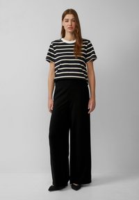 Zwart-wit gestreept shirt met korte mouwen en een ronde halslijn, gecombineerd met loszittende zwarte wijde broek en puntige zwarte flats.