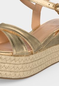 Χρυσό μεταλλικό πλατφόρμα σάντουαλ με πλεκτή σόλα από γιούτα και ρυθμιζόμενο λουράκι στον αστράγαλο, σχέδιο με ανοιχτά δάχτυλα.
