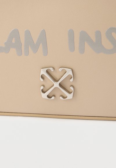 Επιφάνεια μπεζ με μερικό κείμενο γράμματος σε ανοιχτό γκρι πάνω από ένα μικρό, μεταλλικό, συμμετρικό έμβλημα με τέσσερα καμπυλωτά γάντζους που δείχνουν προς τα έξω.