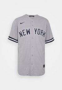 Maillot de baseball gris à boutons avec « NEW YORK » en lettres épaisses, logo Nike noir sur la poitrine droite et poignets de manches rayés noir et blanc.