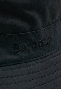 Black fabric bucket hat featuring a stitched "Barbour" logo on a textured band. The material is smooth with a matte finish.