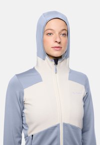 Hooded jack in lichtblauw en crème met een gequilt patroon, voorzien van een ritssluiting aan de voorkant en een logo-detail aan de bovenste linkerkant.
