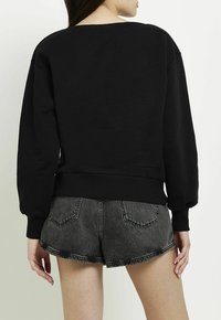 Felpa nera con vestibilità ampia e orlo a coste. Presenta spalle basse e maniche lunghe, abbinata a pantaloncini di denim scuro.