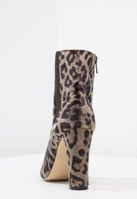 Botín de terciopelo con estampado de leopardo y tacón bloque, panel lateral de elástico negro y cremallera trasera sobre una superficie blanca.