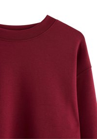 Burgundy sweatshirt med rund halsudskæring, ribstrikkede manchetter og et blødt, tekstureret stof. Har syninger langs sømmene.