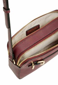Borsa a tracolla in pelle bordeaux con zip dorate. L'interno presenta una fodera chiara e un'etichetta del marchio. Design compatto con forma elegante e strutturata.