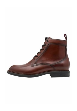 Bottine en cuir marron avec un fini lisse, bout rond, design à lacets et une petite languette à l'arrière. Semelle en caoutchouc noir.