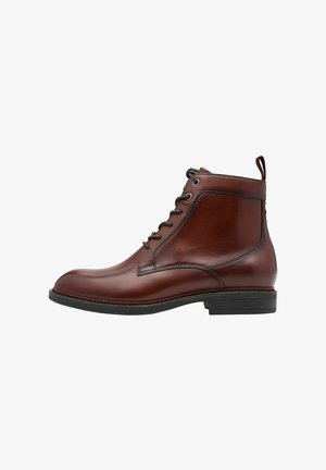 Bottine en cuir marron avec un fini lisse, bout rond, design à lacets et une petite languette à l'arrière. Semelle en caoutchouc noir.