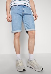 Shorts de mezclilla azul claro con dobladillo vuelto, usados con calcetines blancos y zapatillas deportivas de color claro. Diseño simple y estilo casual.