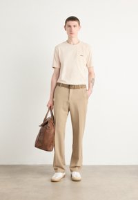 Beige, rövid ujjú ing zsebbel, világosbarna, bő szárú nadrág, barna bőrtáska, fehér sneaker bézs talppal, és minimalista dizájn.