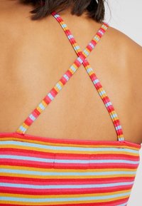 Top sin mangas a rayas con tirantes cruzados en tonos rosa, rojo y azul. Presenta una textura suave y acanalada y un diseño ajustado.