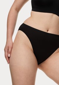 Zwarte bikini-slip van katoenmix met een gladde textuur, hoge uitsnijding en een minimalistisch ontwerp. Elastische tailleband aan de bovenkant.