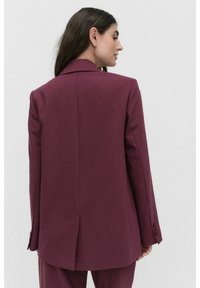 Burgundy skräddarsydd kavaj med slagkrage, strukturerade axlar, slits bak och knäppta manschetter, tillverkad av slätt tyg.