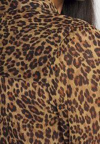 Blusa a stampa leopardata realizzata in un tessuto leggero e trasparente, con tonalità di beige, marrone e macchie scure, e un design con colletto classico.