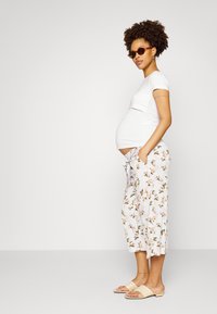 Top ajustado branco, calças cropped florais em azul claro, rosa e verde, com bolsos laterais e laço. Sandálias bejes completam o visual.