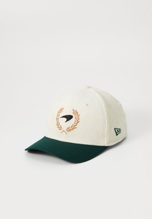 White corduroy cap with a green visor, featuring an embroidered black bird within a brown laurel wreath. Including a logo on the side.