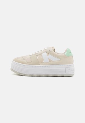 Sneaker platform Calvin Klein con tomaia sintetica beige, branding bianco e accento verde menta sul tallone. Suola in gomma testurizzata.