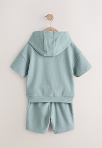 Hele sinine, tekstuuriga kaheosaline komplekt lühikeste varrukate ja lühikestega, millel on kapuuts ja elastne vöökoht. Materjal on pehme ja hingav.