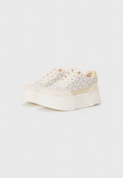 Las zapatillas deportivas blancas de plataforma tienen un upper de tela texturizada con un patrón sutil, detalles en dorado y una entresuela de crema lisa.
